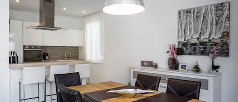 A modern kitchen with white cabinets, a stainless steel range hood, and a wooden dining table with four chairs.