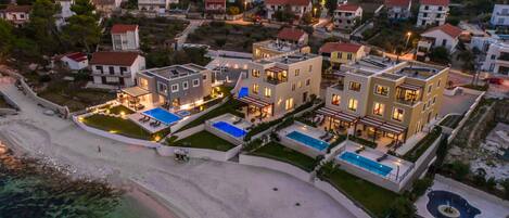 An aerial view of a coastal residential area with modern buildings, a beach, and clear waters.