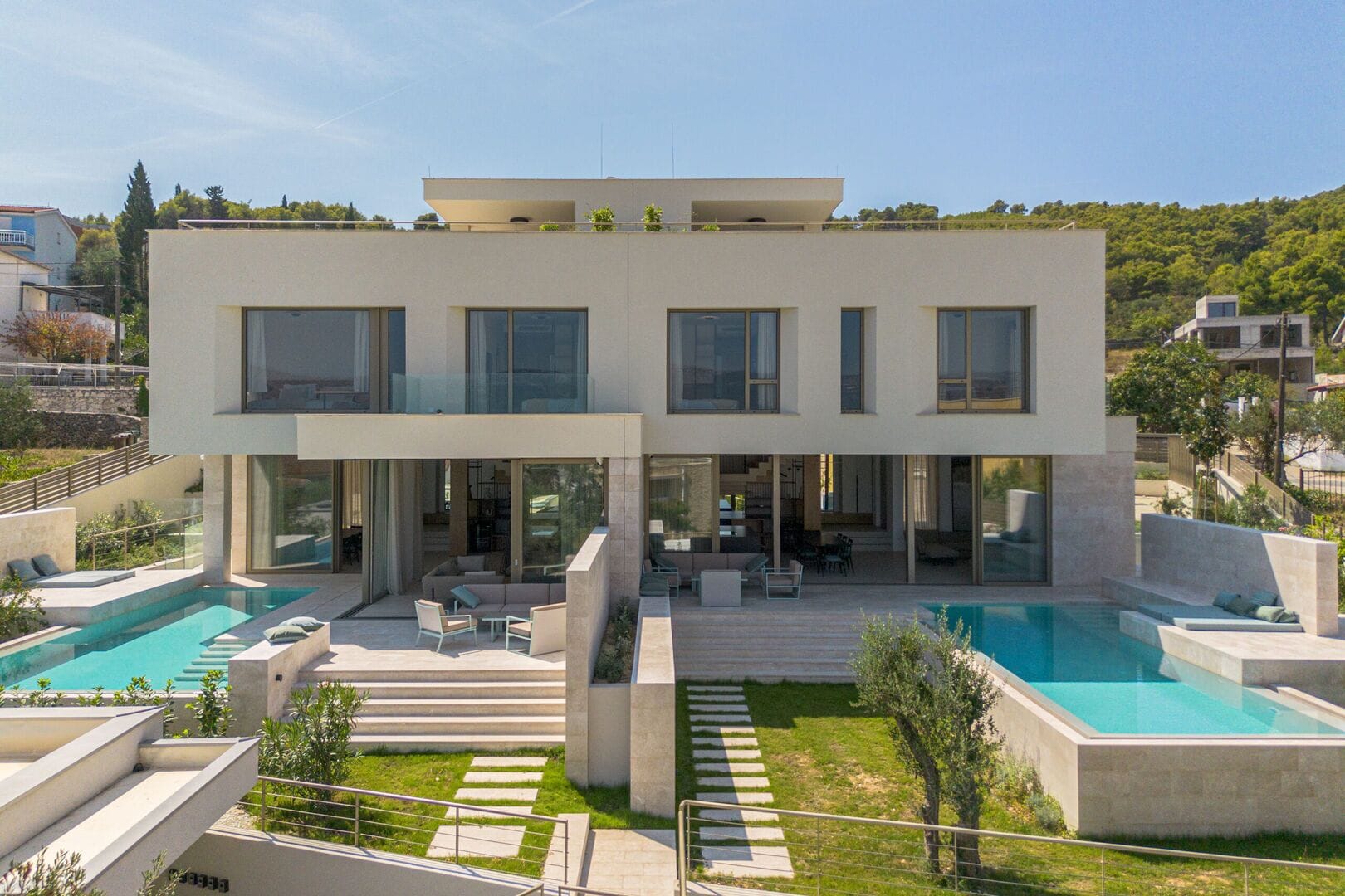 A modern two-story house with a large glass facade, outdoor seating, and a swimming pool.