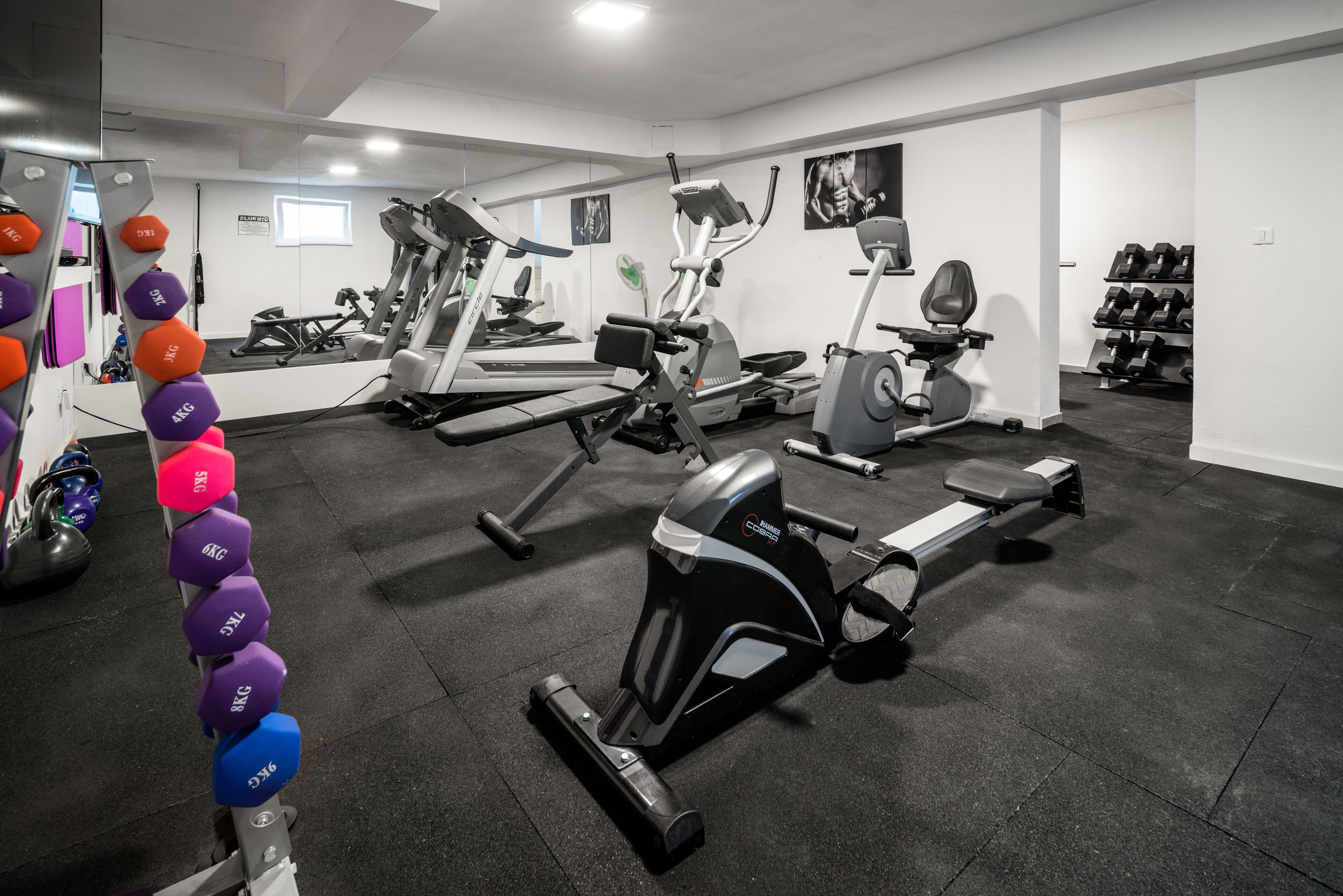 A gym with cardio machines, dumbbells, and a mirror.