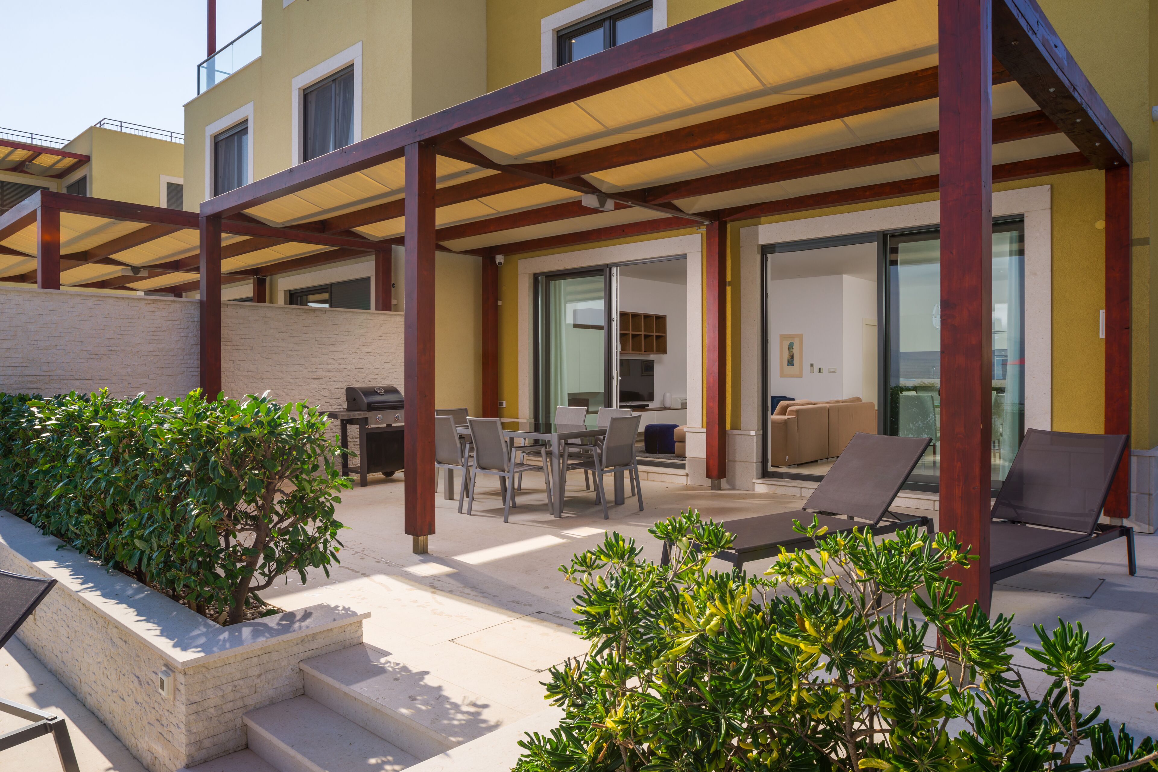 A covered outdoor patio with a dining area, lounge chairs, and a small garden.