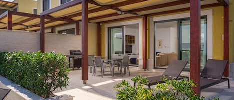 A covered outdoor patio with a dining area, lounge chairs, and a small garden.
