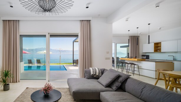 Una sala de estar moderna con un sofá gris, una mesa de centro redonda y vistas a una piscina y montañas.
