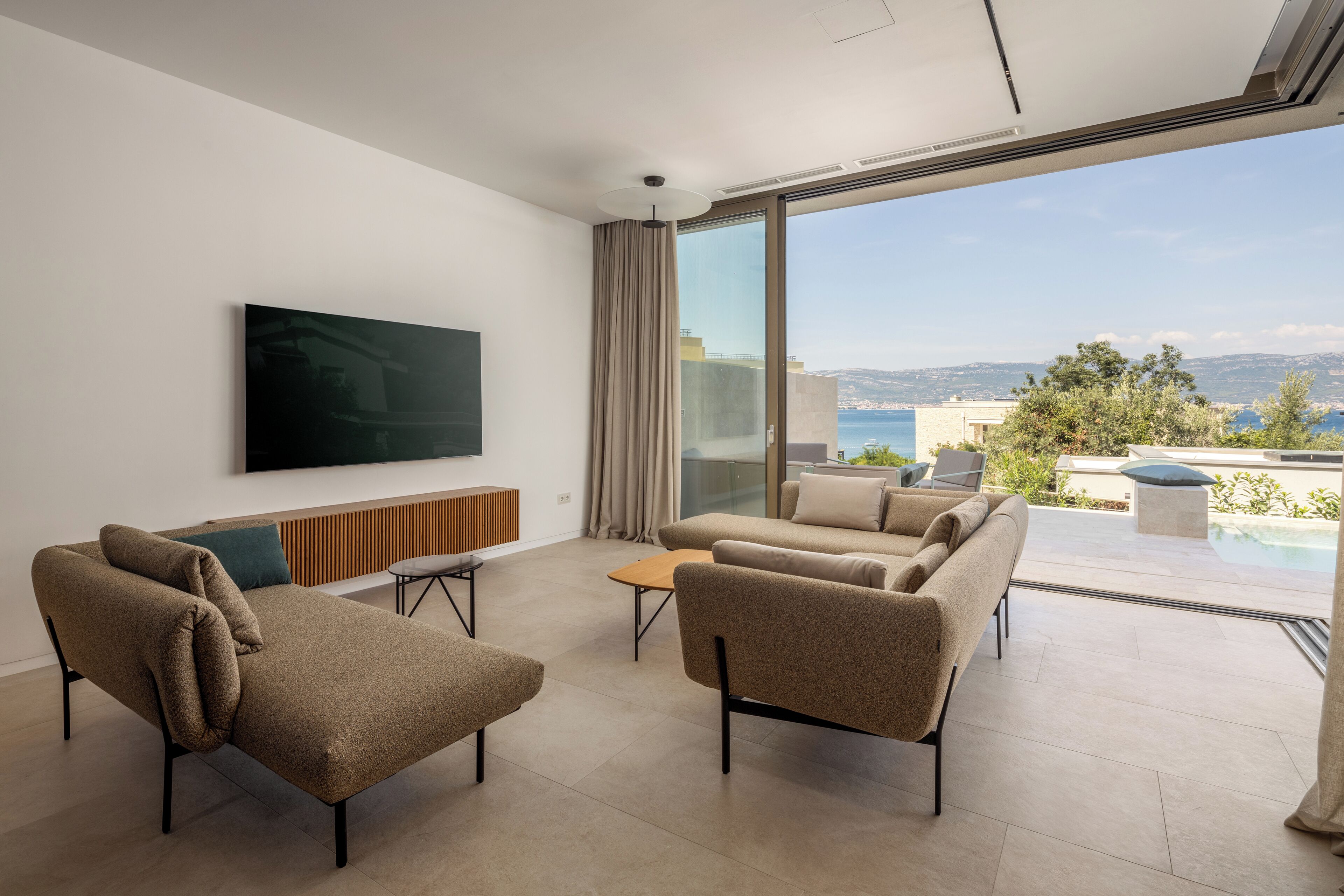Ein modernes Wohnzimmer mit Flachbildfernseher, einer Couch, einem Couchtisch und Blick aufs Meer.