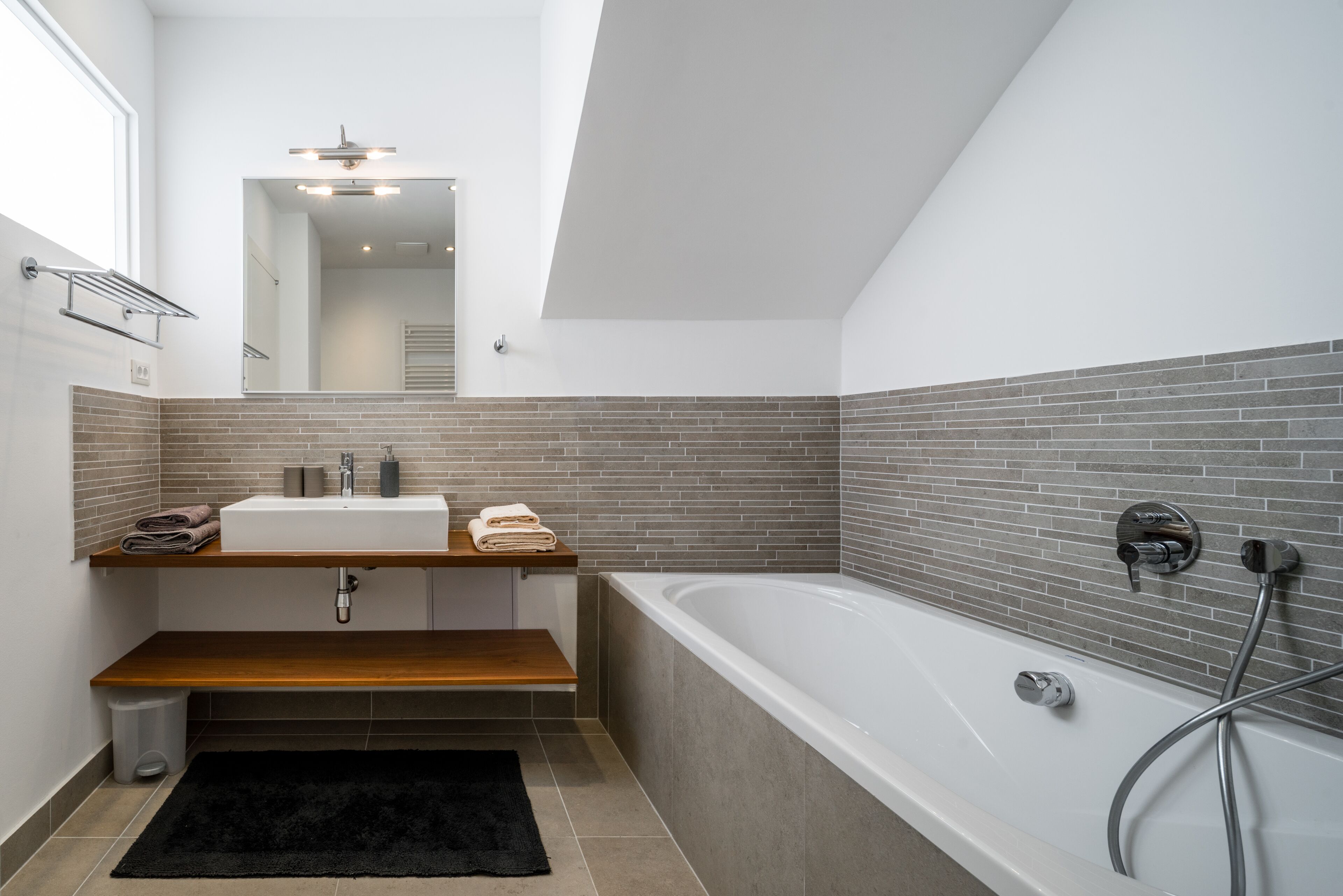 A modern bathroom with a large bathtub, a wooden vanity, and a tiled backsplash.
