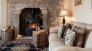 A cozy living room with a stone fireplace, a sofa with floral cushions, a wicker basket, and a patterned rug. - Bartlehill Cottage, Idyllic Pet Friendly Cottage, Beautiful Scottish Borders (Coldstream)