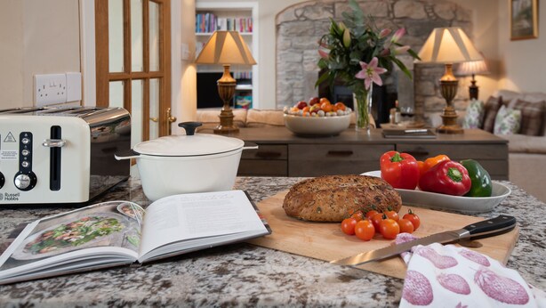 A kitchen counter with a loaf of bread, a cutting board with tomatoes, a knife, a book, and a toaster. - Bartlehill Cottage, Idyllic Pet Friendly Cottage, Beautiful Scottish Borders (Coldstream)