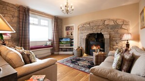 A cozy living room with a stone fireplace, comfortable sofas, a television, and a bookshelf. - Bartlehill Cottage, Idyllic Pet Friendly Cottage, Beautiful Scottish Borders (Coldstream)