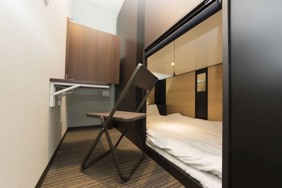 A compact hotel room with a foldable desk, a single bed, and a wardrobe.