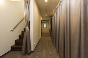 Ein Hotelgang mit Teppichboden, einer Treppe links und Vorhängen an beiden Seiten.
