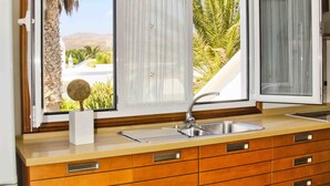 A kitchen with a large window, a sink, and wooden cabinets. - CASA JUANITA by Buenavilla | Exclusive apartment with private pool (Puerto Calero)