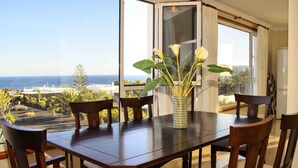 A dining area with a table and chairs, a vase with flowers, and a view of the ocean. - CASA JUANITA by Buenavilla | Exclusive apartment with private pool (Puerto Calero)