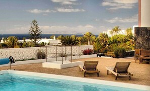 Área de piscina no terraço com espreguiçadeiras, vista para o oceano e paisagismo tropical.