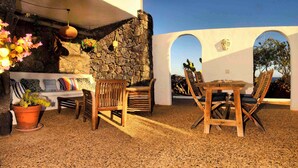 An outdoor patio with a stone wall, wooden furniture, and potted plants. - CASA JUANITA by Buenavilla | Exclusive apartment with private pool (Puerto Calero)