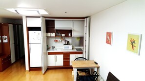 A compact kitchen with a microwave, sink, and cabinets, a dining table with chairs, and a refrigerator. - Seoul Stay (Seoul)