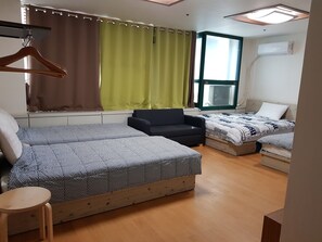 A room with two beds, a sofa, a wooden table, and a window with curtains. - Seoul Stay (Seoul)