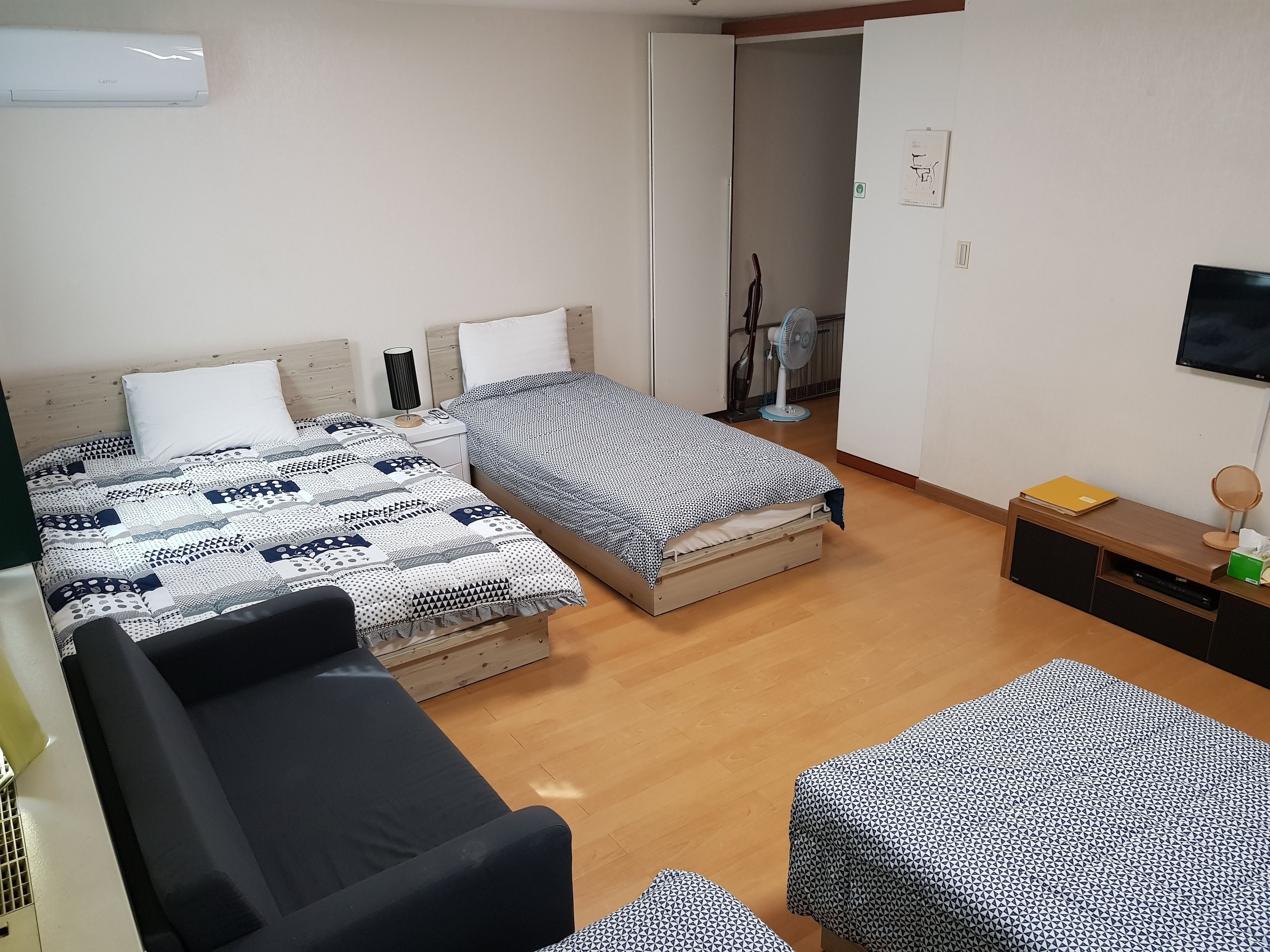 A bedroom with two beds, a sofa, a TV, and a desk with a mirror and lamp.