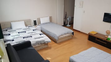 A bedroom with two beds, a sofa, a TV, and a desk with a mirror and lamp.