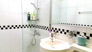 A bathroom with a white sink, a mirror, and a shower. There are toiletries on a shelf and a towel rack.