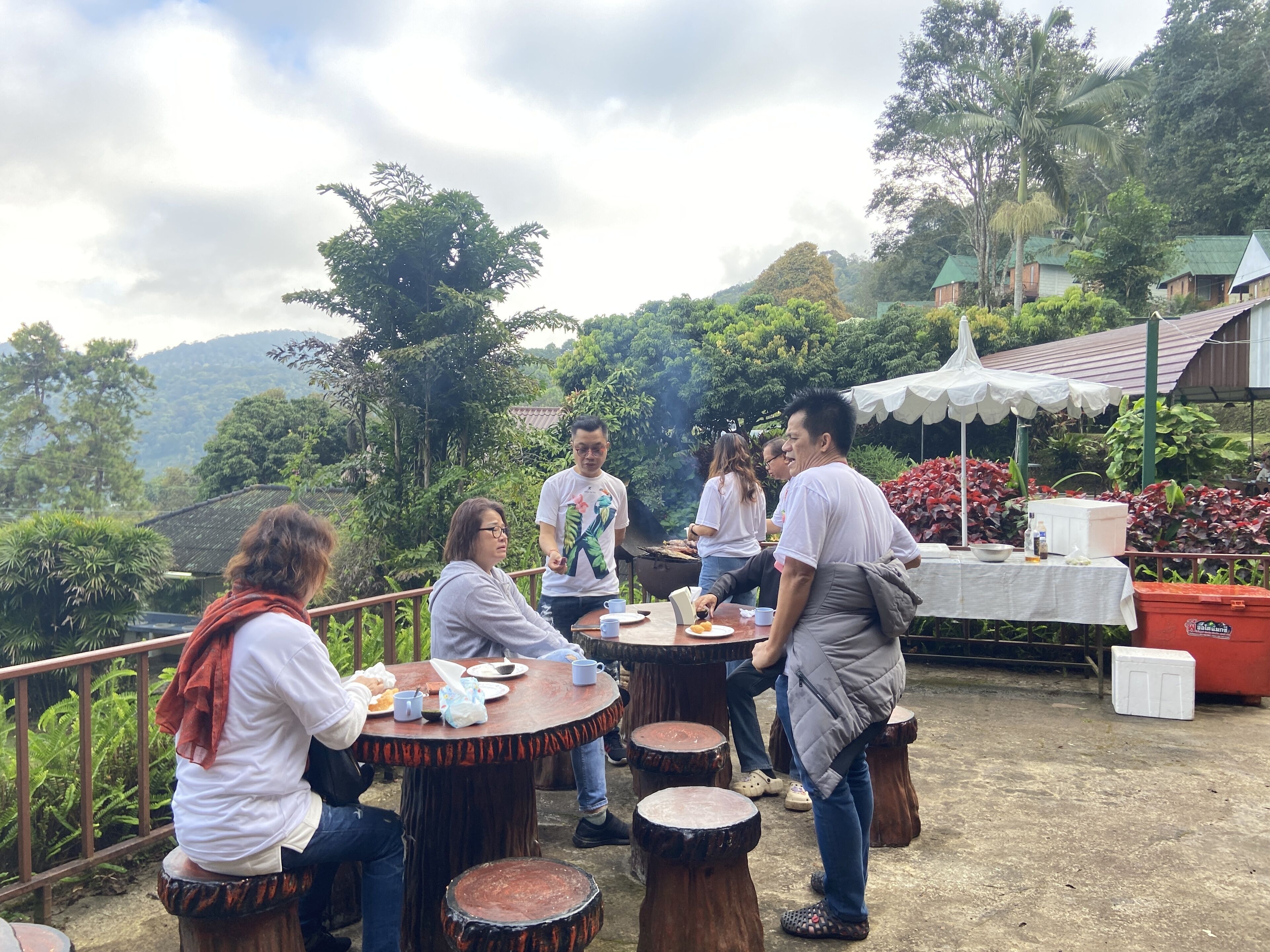 Um grupo de pessoas jantando ao ar livre, com uma paisagem montanhosa ao fundo.