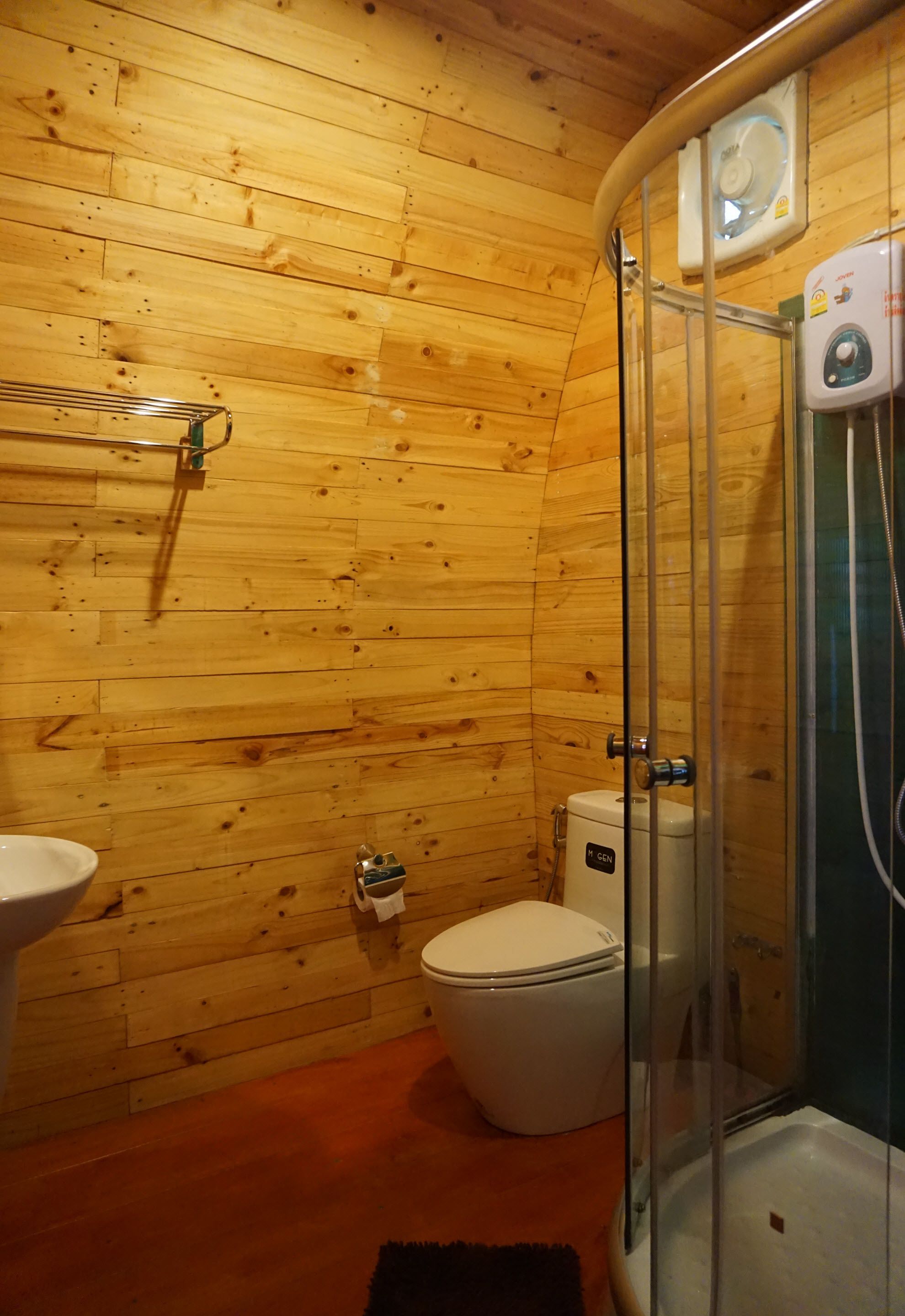Un baño con paneles de madera, que incluye inodoro, lavamanos y ducha con mampara de vidrio.