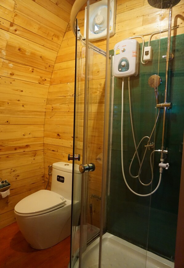 Un baño con paneles de madera, ducha con cerramiento de vidrio, inodoro y calentador de pared.