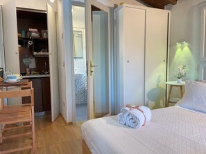 Una camera d'albergo con un letto, una sedia in legno, un tavolino con una lampada e un armadio.