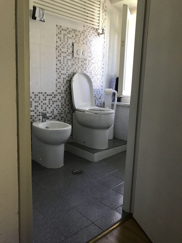 Une salle de bain avec deux toilettes, un bidet et un espace douche.