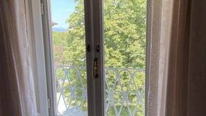 Una habitación con ventana que da a un balcón con barandilla blanca y vegetación.