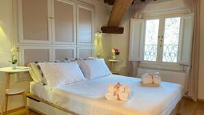 Una cama bien hecha con toallas, una mesita de noche con un florero y una ventana con vistas al verdor.