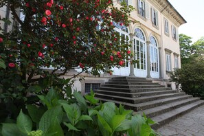 Un bâtiment doté d’une entrée imposante, d’un escalier menant aux portes principales et d’une végétation luxuriante en premier plan.