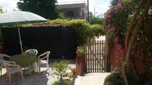 A patio area with a table and chairs, a wooden gate, and a small garden. - La Coccinella (Massarosa)