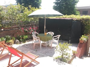 A patio with a table and chairs under a large umbrella, surrounded by potted plants and a brick wall.
