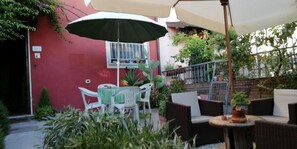 An outdoor seating area with a table and chairs, a potted plant, and a red wall. - La Coccinella (Massarosa)