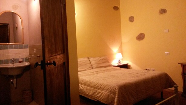 A bedroom with a bed, a bedside table with a lamp, and a bathroom with a sink and mirror. - La Coccinella (Massarosa)