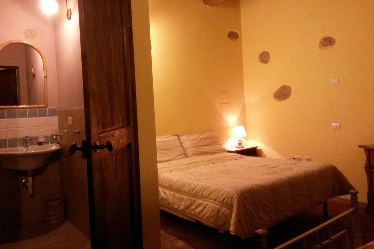 Une chambre à coucher avec un lit, une table de chevet avec une lampe, et une salle de bain avec un lavabo et un miroir.