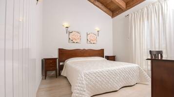A bedroom with a wooden ceiling, a bed with a quilted white duvet, two wall-mounted lamps, and a wooden nightstand.