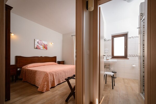A bedroom with a bed, a nightstand, a painting on the wall, and a bathroom with a sink, mirror, and window. - La Dimora di Federico (Avigliano)
