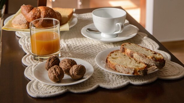 A breakfast setting with croissants, a glass of orange juice, a cup, and walnuts on a table.