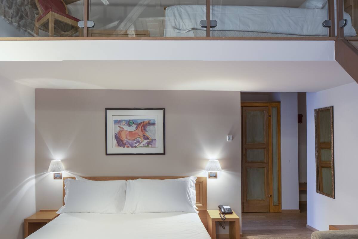 Ein Schlafzimmer mit Bett, Nachttischlampen, einem Nachttisch, einem gerahmten Bild an der Wand und einem Balkon mit Stuhl.