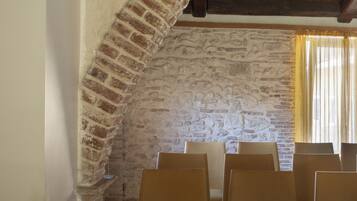 A room with a stone wall, wooden ceiling beams, and several chairs arranged for seating.