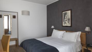 Ein Schlafzimmer mit einem Bett, Nachttischlampen, einem Schreibtisch mit Stuhl, einem Spiegel und einem Bild an der Wand.