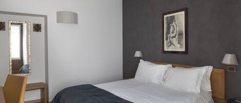 Un dormitorio con cama, lámparas de noche, un escritorio con silla, un espejo y un cuadro en la pared.