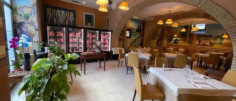 A restaurant with a central dining area, a large potted plant, and a mural on the wall.