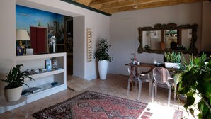 A living room with a cityscape mural, a large mirror, and a dining area with clear chairs. - Hotel 99 Cannelle (L'Aquila)