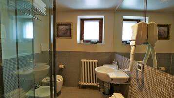 Een badkamer met een glazen douchecabine, toilet, wastafel en radiator.