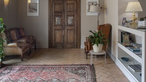 A cozy interior with a wooden door, leather armchairs, a patterned rug, and a bookshelf with books and decorative items. - Hotel 99 Cannelle (L'Aquila)