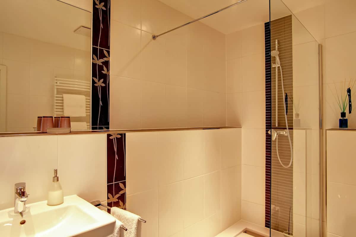 Un baño moderno con ducha envuelta en vidrio, un lavamanos blanco y un espejo que refleja el cuarto.