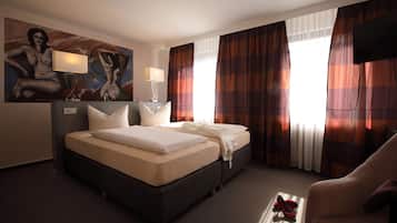 A hotel room with a bed, two bedside lamps, a TV, and a painting on the wall.