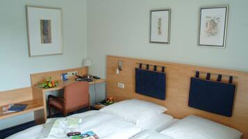 A hotel room with two beds, a desk, a chair, and framed artwork on the walls.